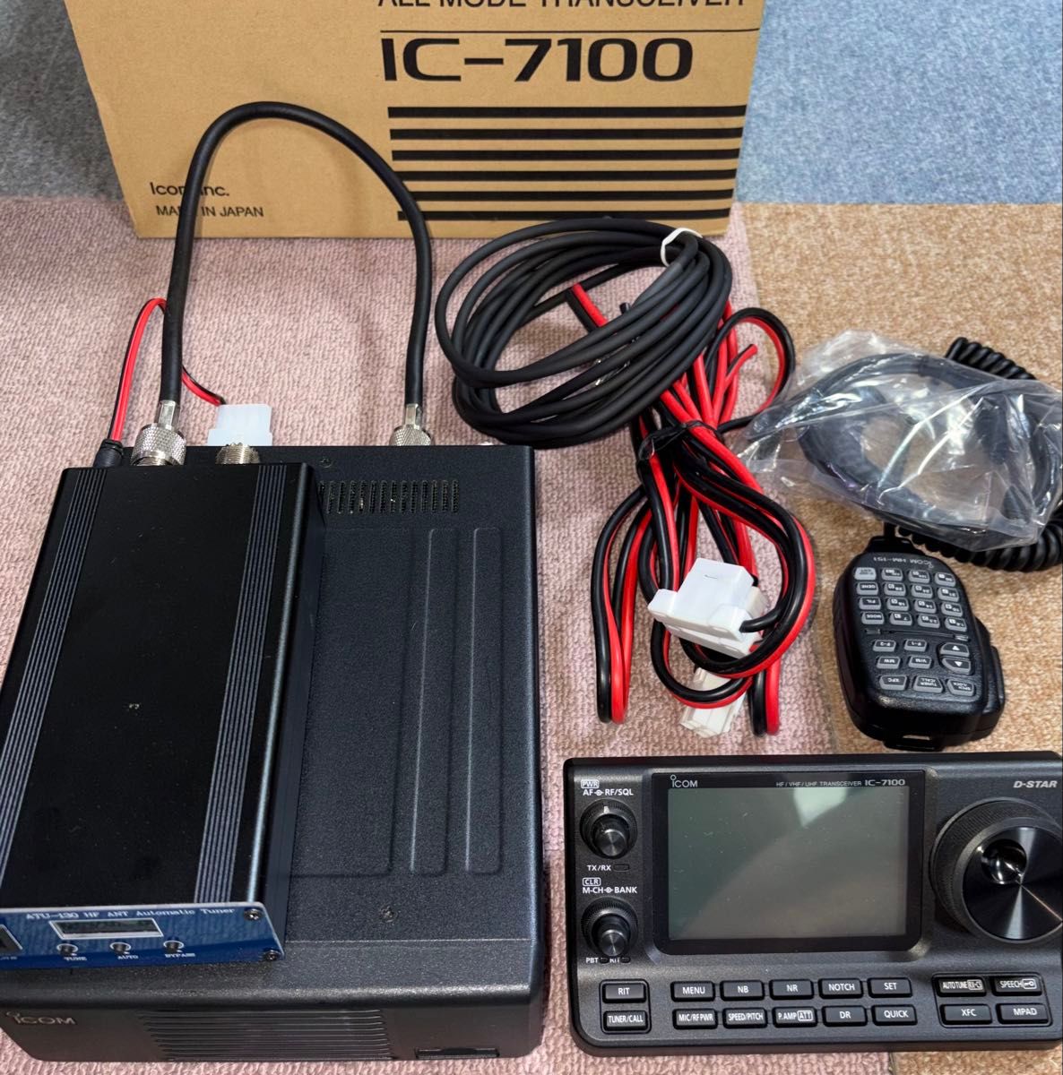 IC-7100 transceiver control head, power cables, microphone, and accessories displayed with the product box in the background.