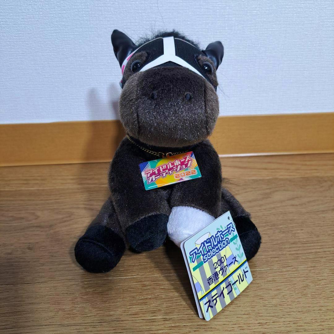 Front view of the Idol Horse M-size Stay Gold Hong Kong Vase plush sitting on a wooden floor with its tag visible.