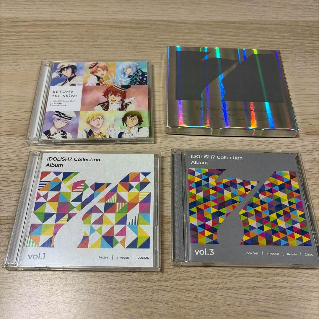 Photograph of three IDOLiSH7 CD cases and a holographic box arranged on a wooden surface.