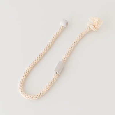 A cream-colored braided curtain tassel with a rectangular slider, a round bead, and a frayed end on a white background.