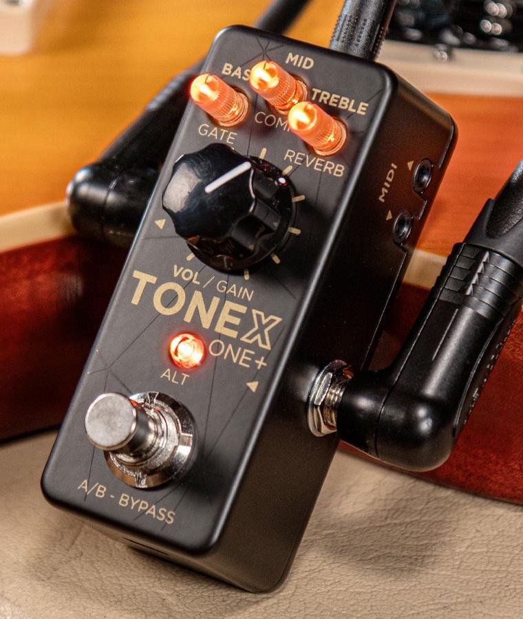 Close-up photo of the IK Multimedia TONEX One+ guitar effects pedal showing knobs, a footswitch, and connected cables.