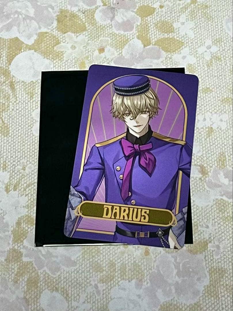 Photo of a trading card showing the illustrated character DARIUS in a purple uniform with the name "DARIUS" on a gold plate, placed on a black sleeve on a floral surface.