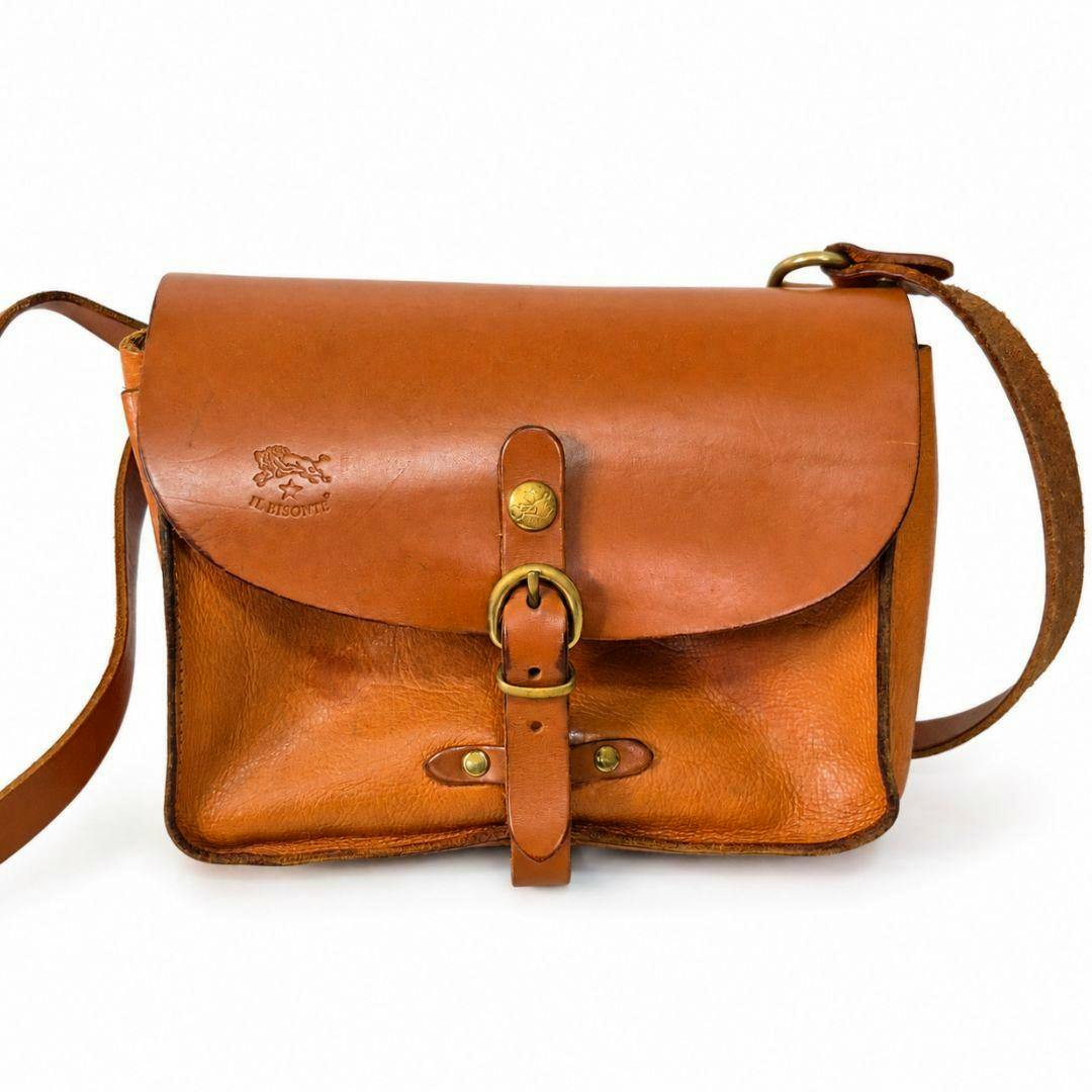Front view of an IL BISONTE tan leather shoulder bag with a flap, buckle strap, and embossed logo.