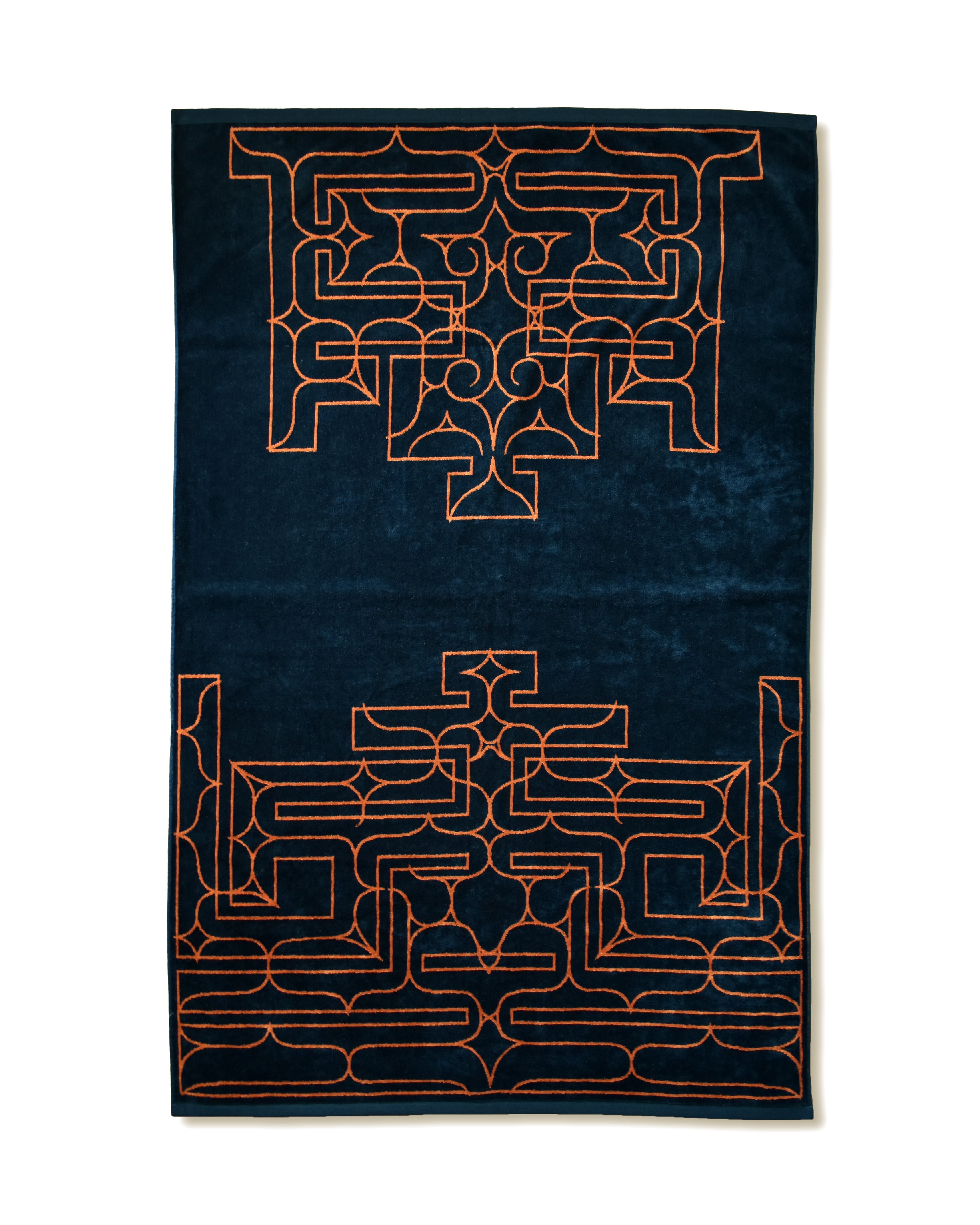 A navy Imabari towel blanket with an orange Ainu-style pattern laid flat.