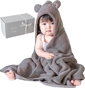 A baby wearing a brown hooded towel with bear ears, draped over them next to a gift box.
