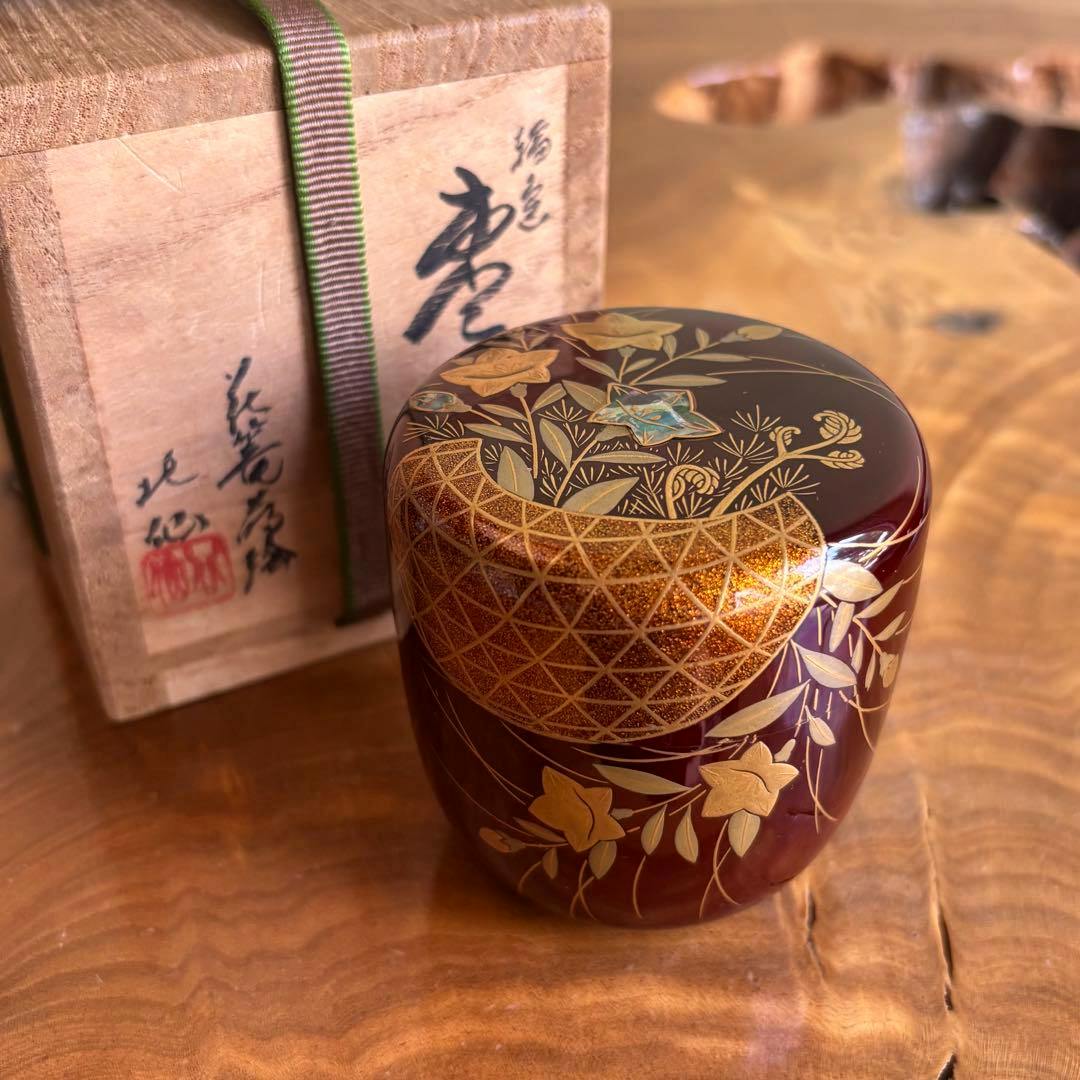A Wajima lacquer natsume tea caddy decorated with gold flower-basket maki-e shown with its wooden tomobako box.