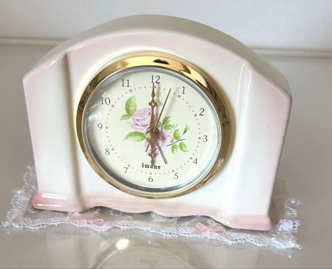 Ceramic alarm clock with a pink rose dial and gold bezel displayed on lace.