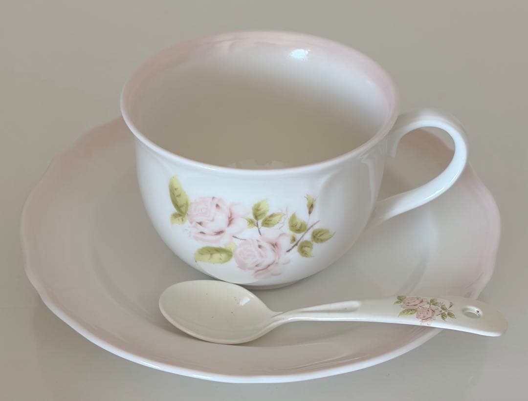 Porcelain cup and saucer with pink rose design and matching spoon.