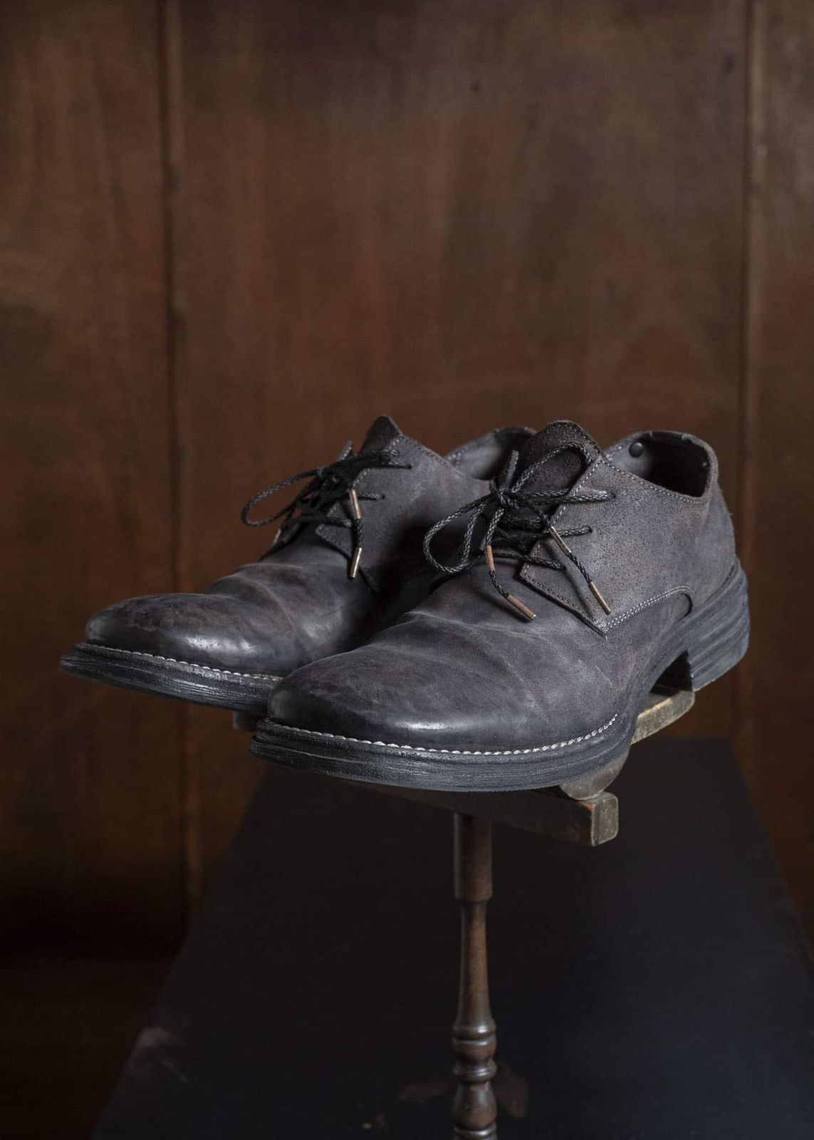 A pair of leather lace-up low-cut shoes displayed on a small stand against a wooden background.