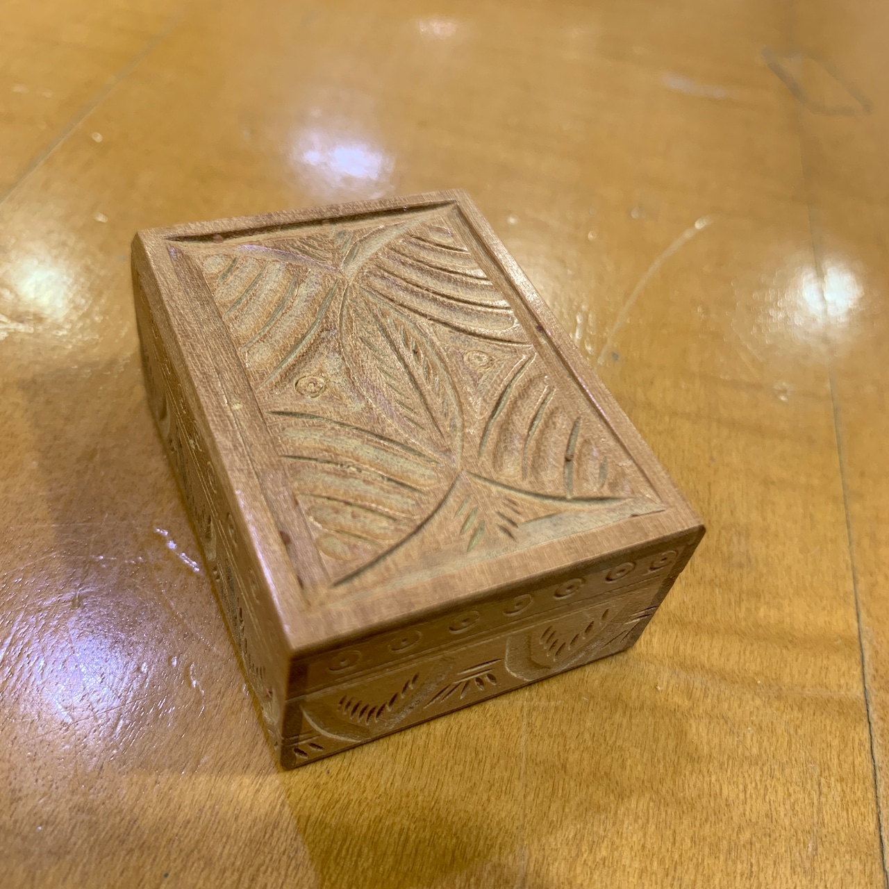Small carved wooden case with leaf-like patterns sitting on a wooden surface.