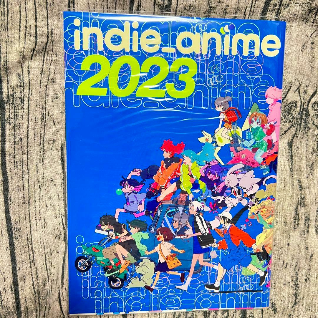 Front cover of the indie_anime 2023 book showing a bright blue illustrated cover with many colorful anime characters and the title "indie_anime 2023".