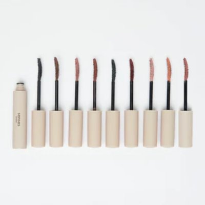 Several opened mascara tubes with wands showing different mascara shades arranged in a row on a white background.
