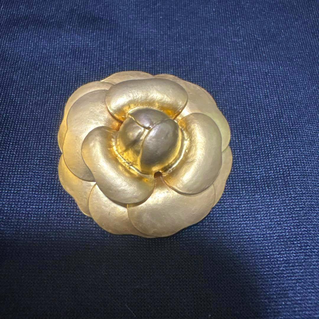 Gold camellia-shaped brooch photographed against dark blue fabric.