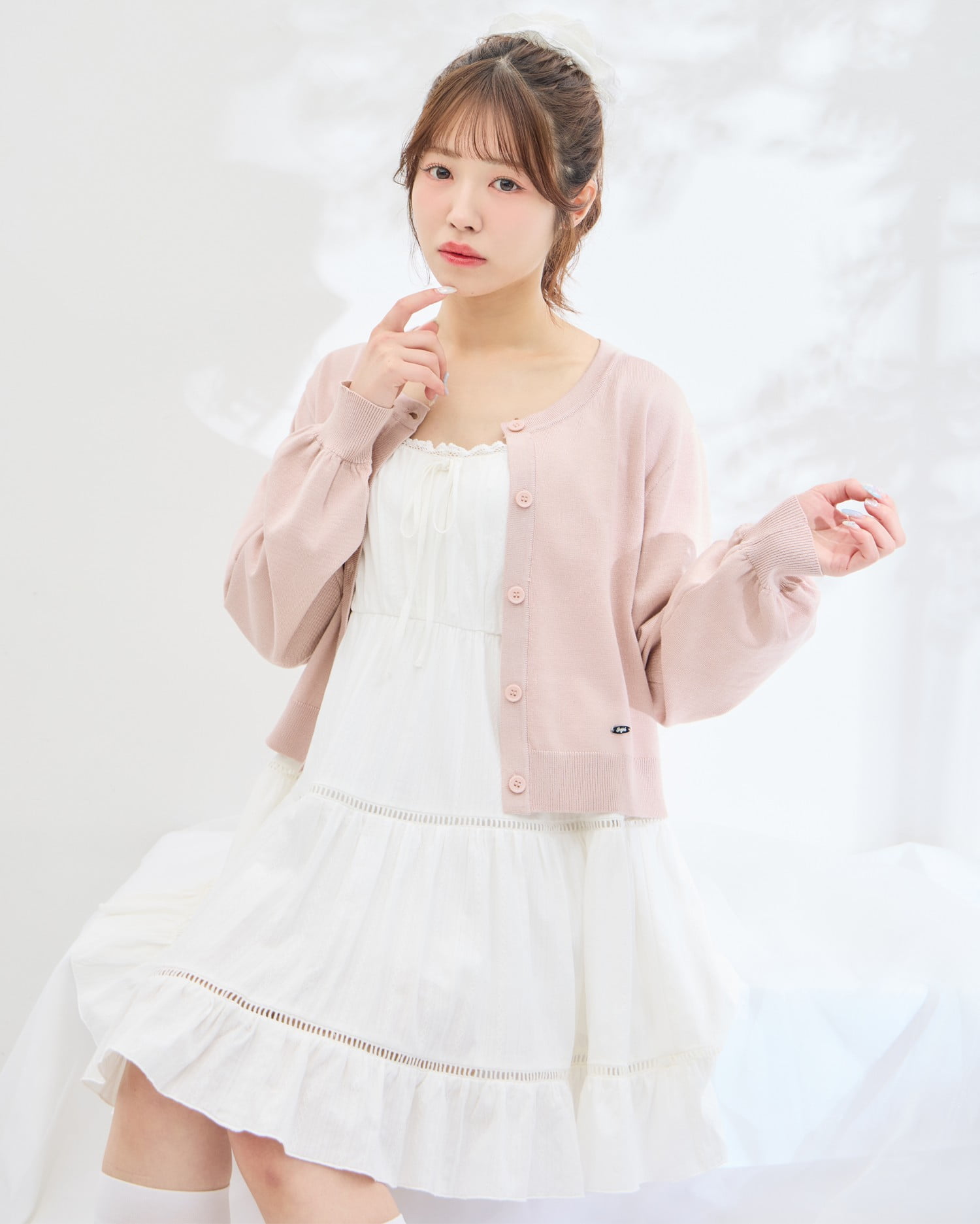 Model wearing the white lace tiered mini camisole dress styled with a pink cardigan.