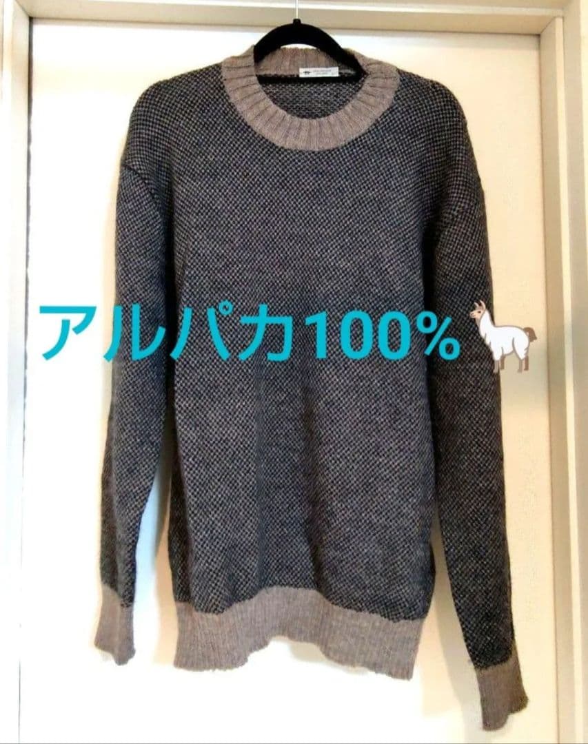 Front view of the men's alpaca knit sweater (Inis Meáin) hanging on a black hanger against a light-colored door, with a Japanese "アルパカ100%" text overlay.