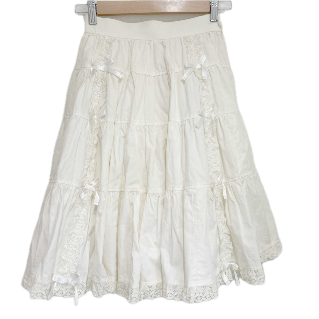 White tiered women's skirt with lace trim and ribbon bows shown on a hanger.