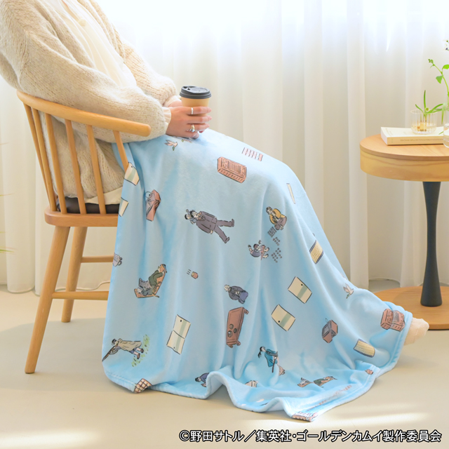 Light blue polyester big blanket with character prints draped over a seated person in a wooden chair.