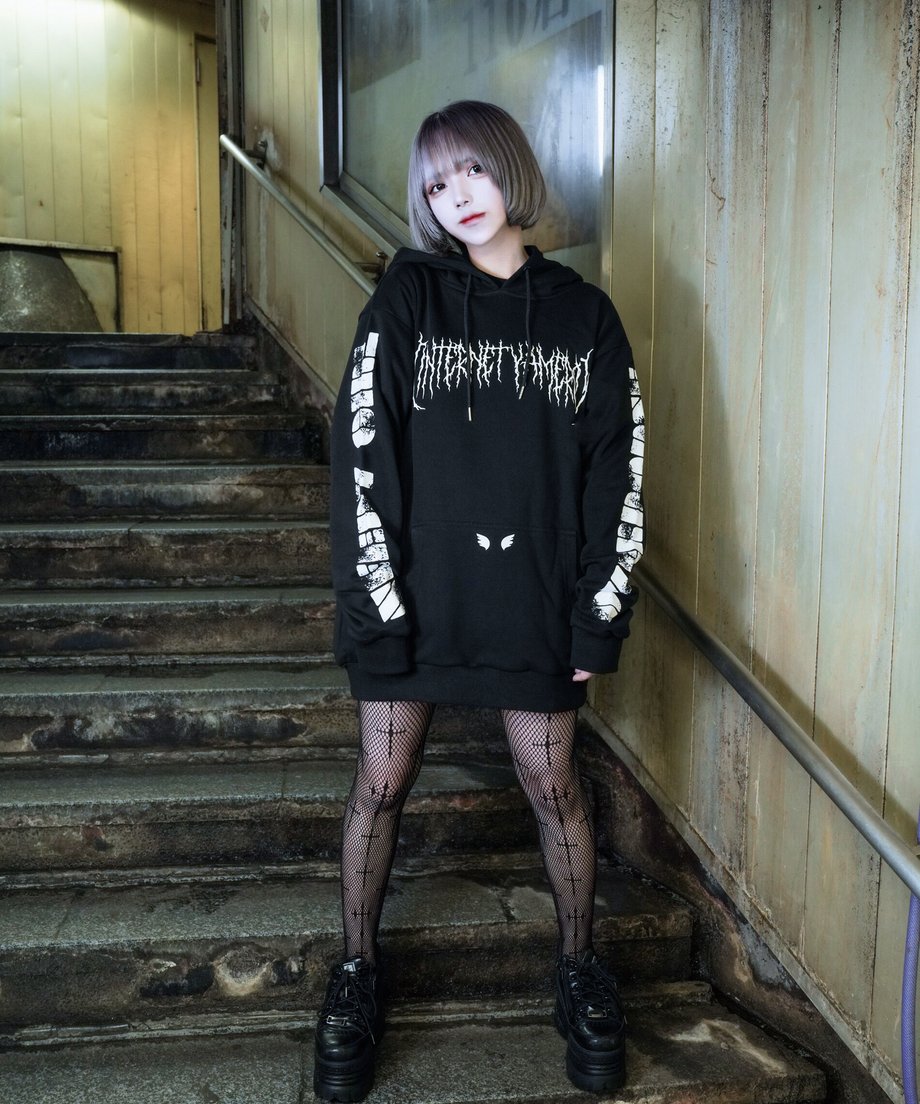 Model wearing a black pullover hoodie (sweatshirt) showing the front printed text and graphics and printed sleeves.