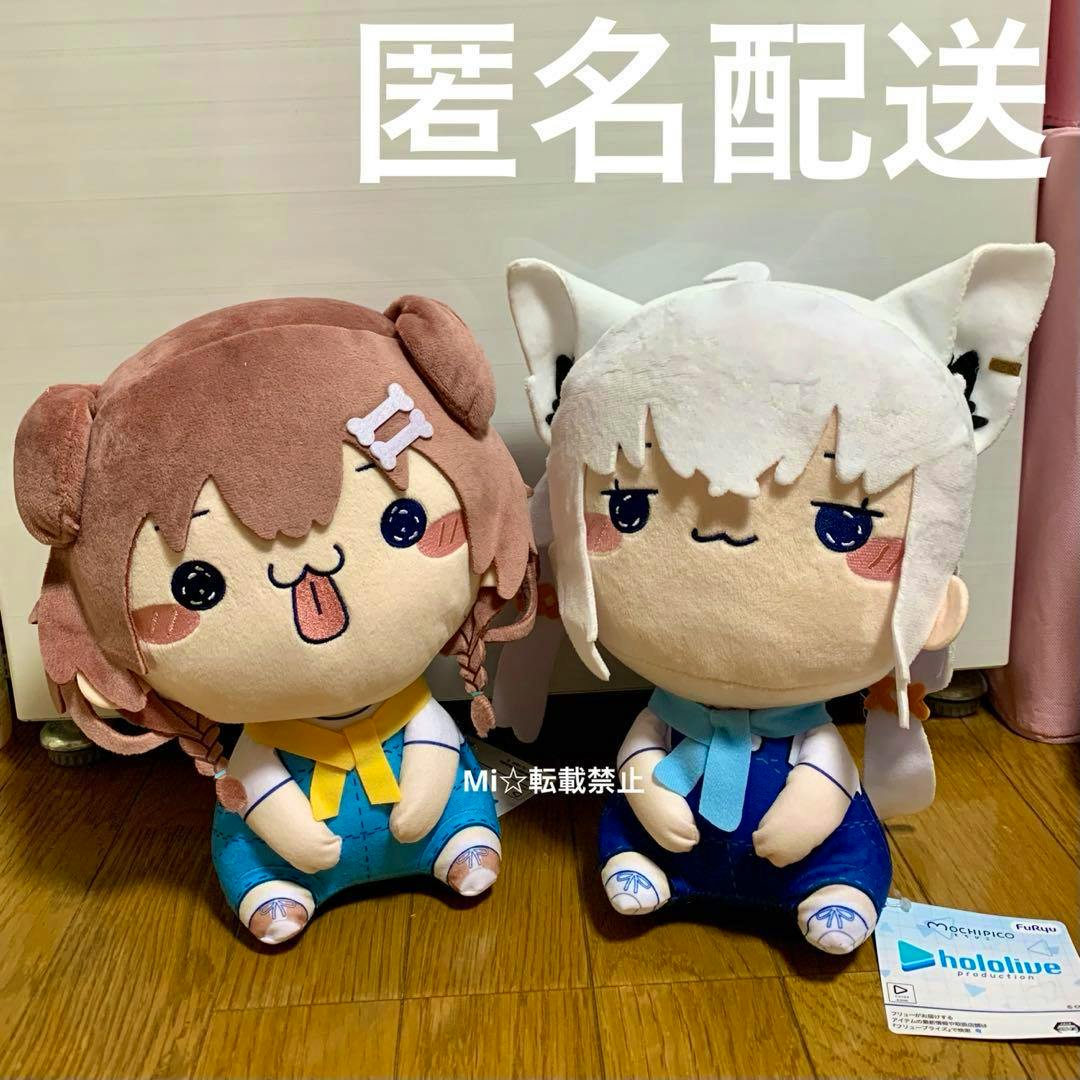 Two mochipico BIG plush toys of Inugami Korone (brown-haired) and Shirakami Fubuki (white-haired) sitting side by side on a wooden floor with a Hololive tag visible.