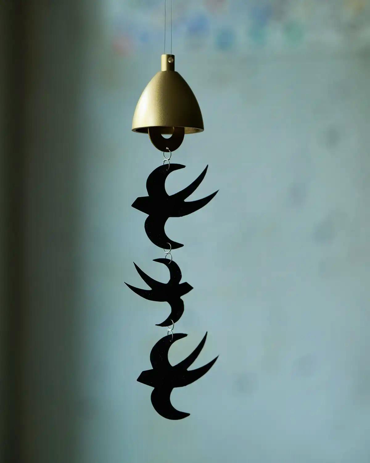 A hanging iron wind chime with a gold bell top and three black swallow-shaped pieces linked vertically.