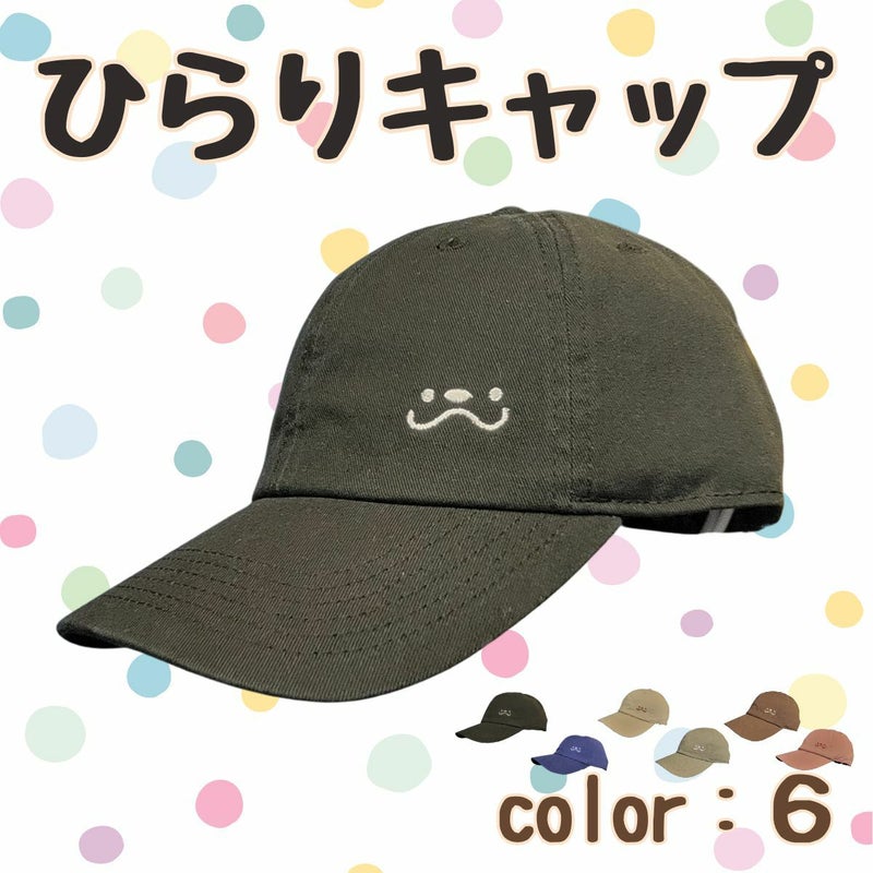 A dark-colored cotton baseball cap with a small embroidered face on the front against a pastel polka-dot background.