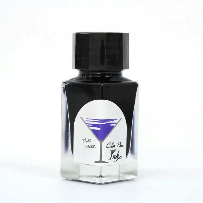 A glass bottle of fountain pen ink labeled "Blue Moon" with a purple cocktail-glass graphic on the front.