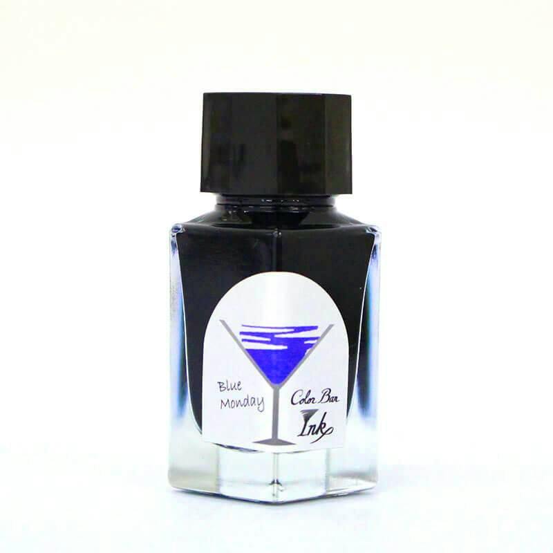 A bottle of fountain pen ink labeled "Blue Monday" Color Bar Ink with a martini-glass logo showing blue ink.