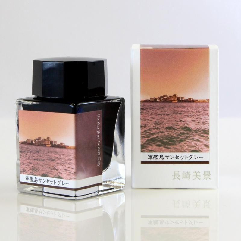 A fountain pen ink bottle labeled "軍艦島サンセットグレー" displayed next to its matching box, both showing a sunset seascape label.