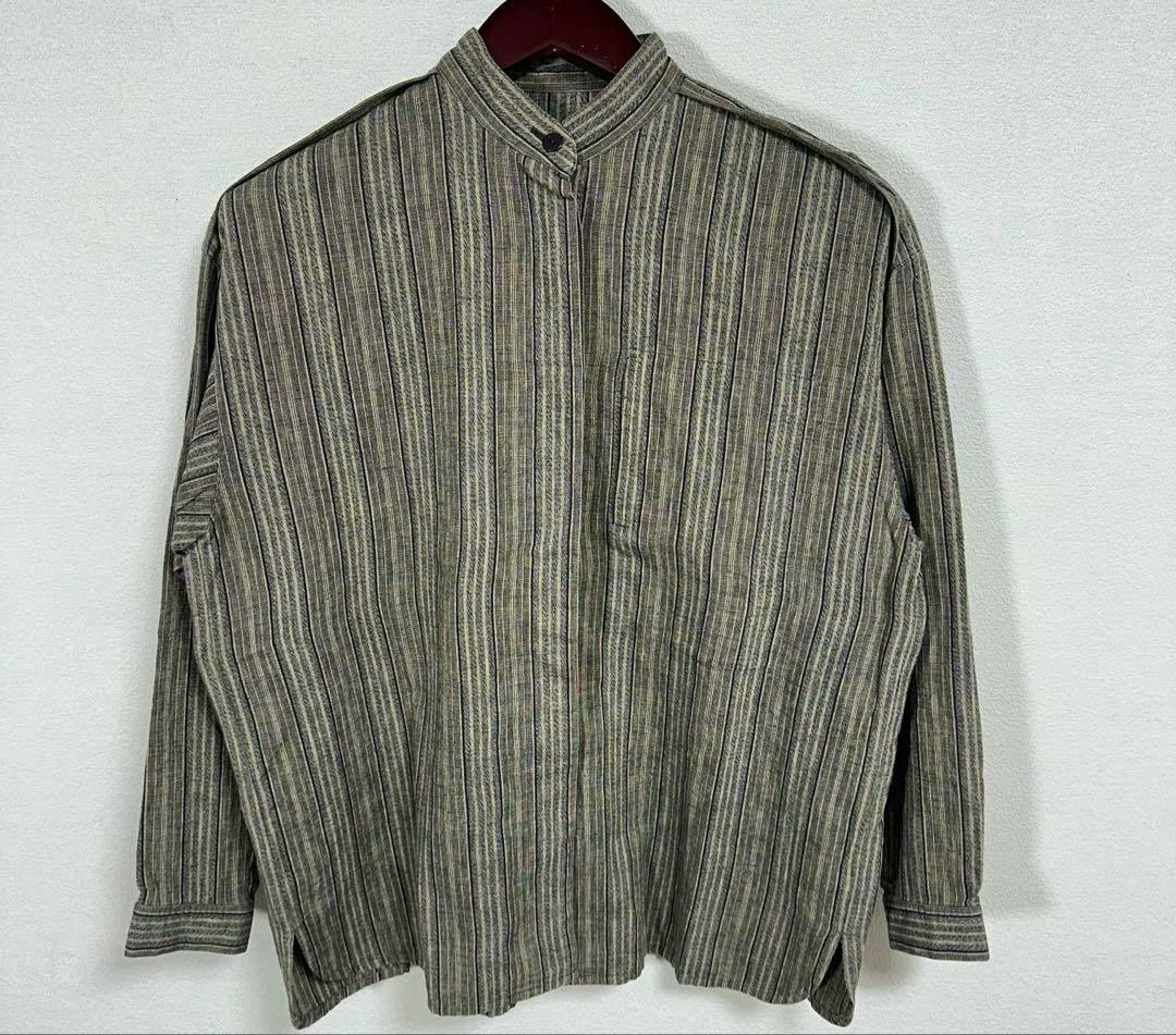 Front view of an Issey Miyake men's cotton no-collar shirt with vertical stripes hanging on a hanger against a plain background.