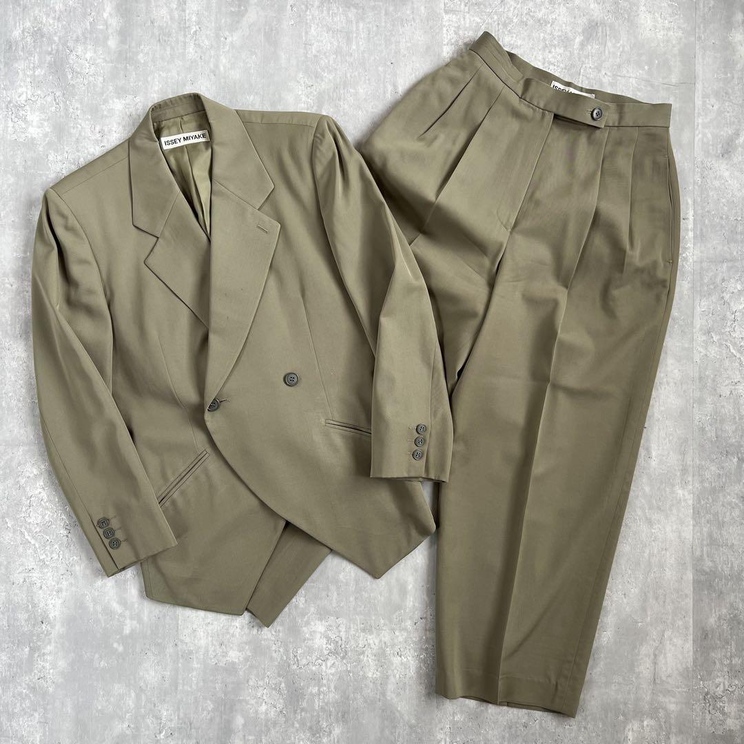 Olive-green Issey Miyake wool jacket and matching trousers laid flat on a gray background.