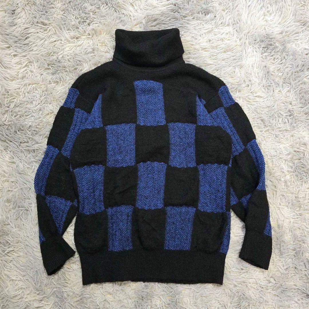Blue and black checkered turtleneck sweater laid flat on a light shag rug.