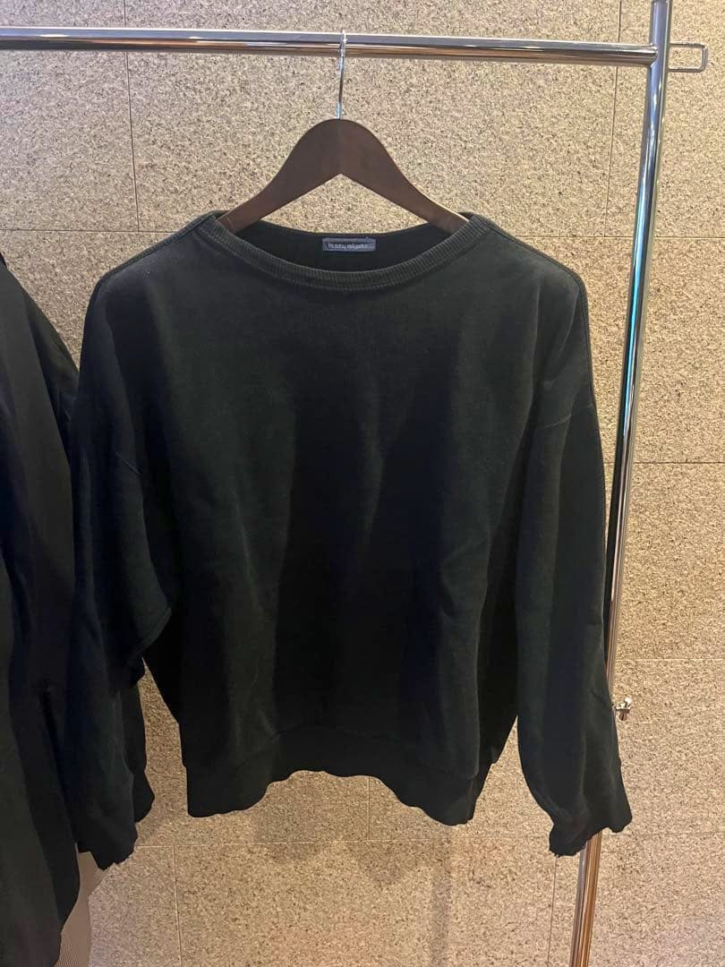 Black Issey Miyake Men crewneck sweatshirt hanging on a wooden hanger on a clothing rack.