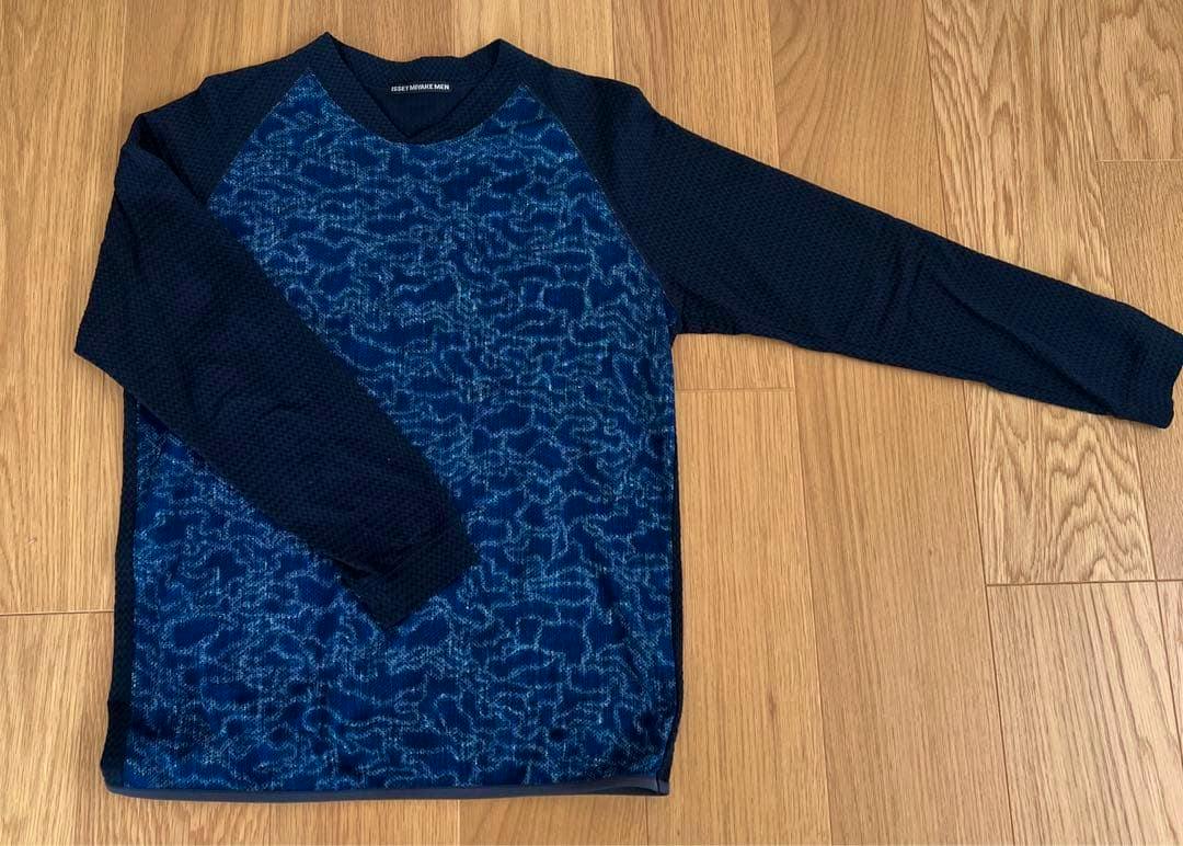 Blue ISSEY MIYAKE MEN long-sleeve polyester sweater laid flat on a wooden floor, showing a patterned front and solid sleeves.