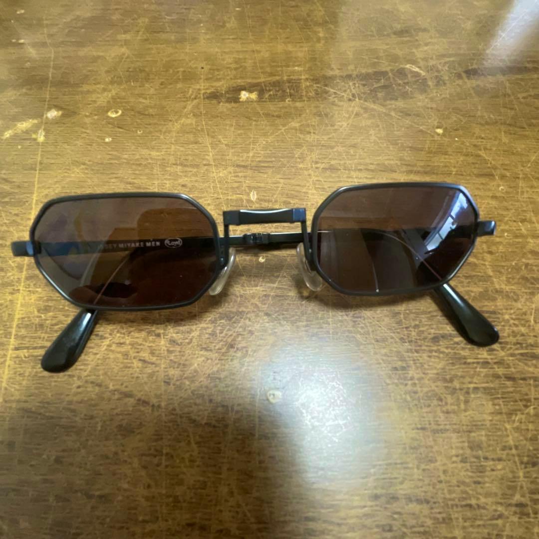 ISSEY MIYAKE MEN foldable sunglasses (Loyd) with dark lenses and a black frame lying on a wooden surface.