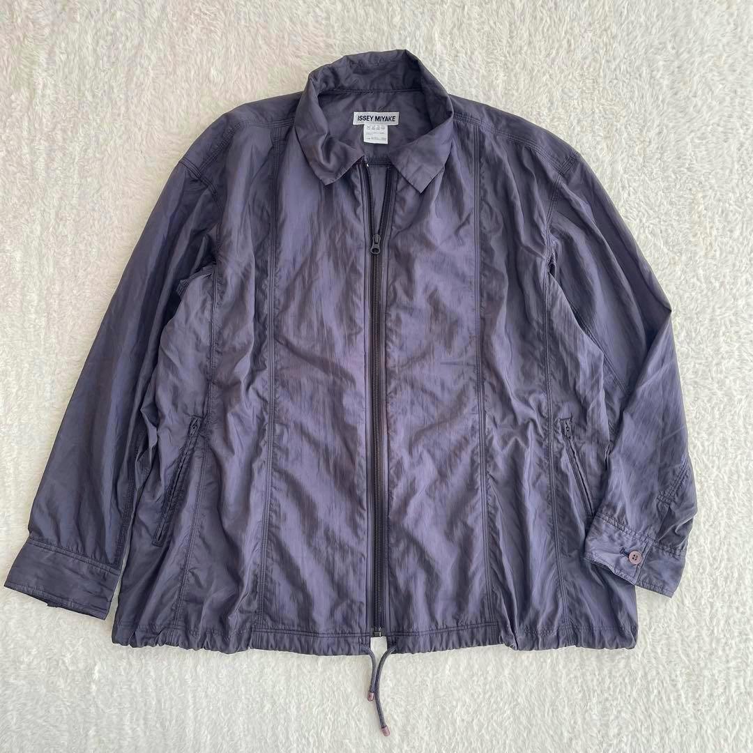 ISSEY MIYAKE men's nylon jacket laid flat showing the front with zipper and hem drawstring on a light textured background.