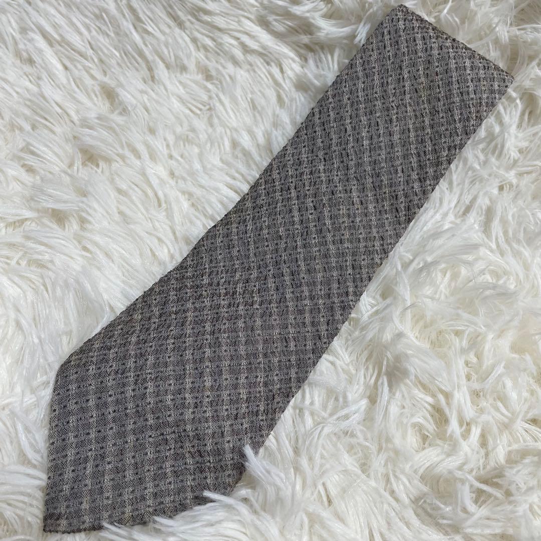 A grey patterned ISSEY MIYAKE silk necktie laid flat on a white fluffy surface.