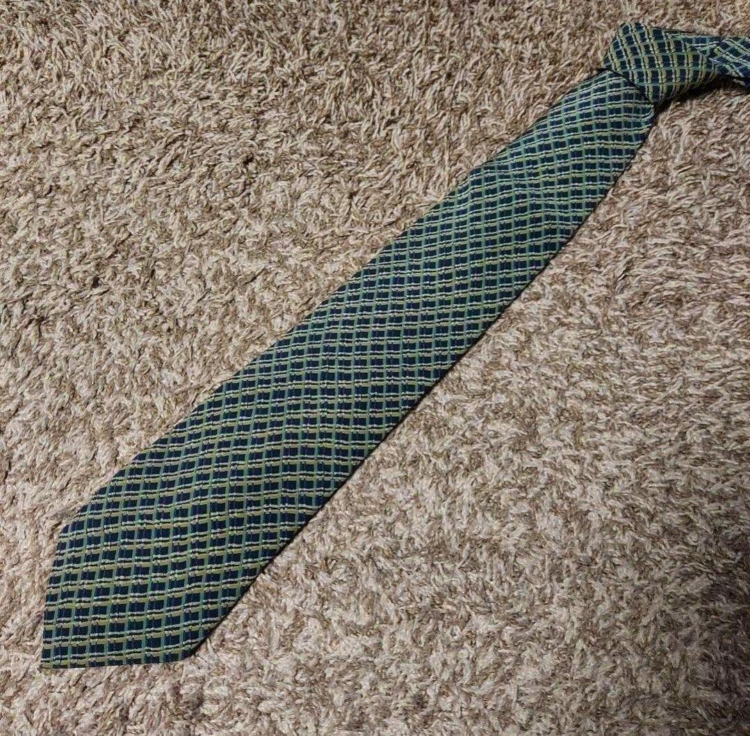 A green patterned silk necktie laid flat on a beige carpet.