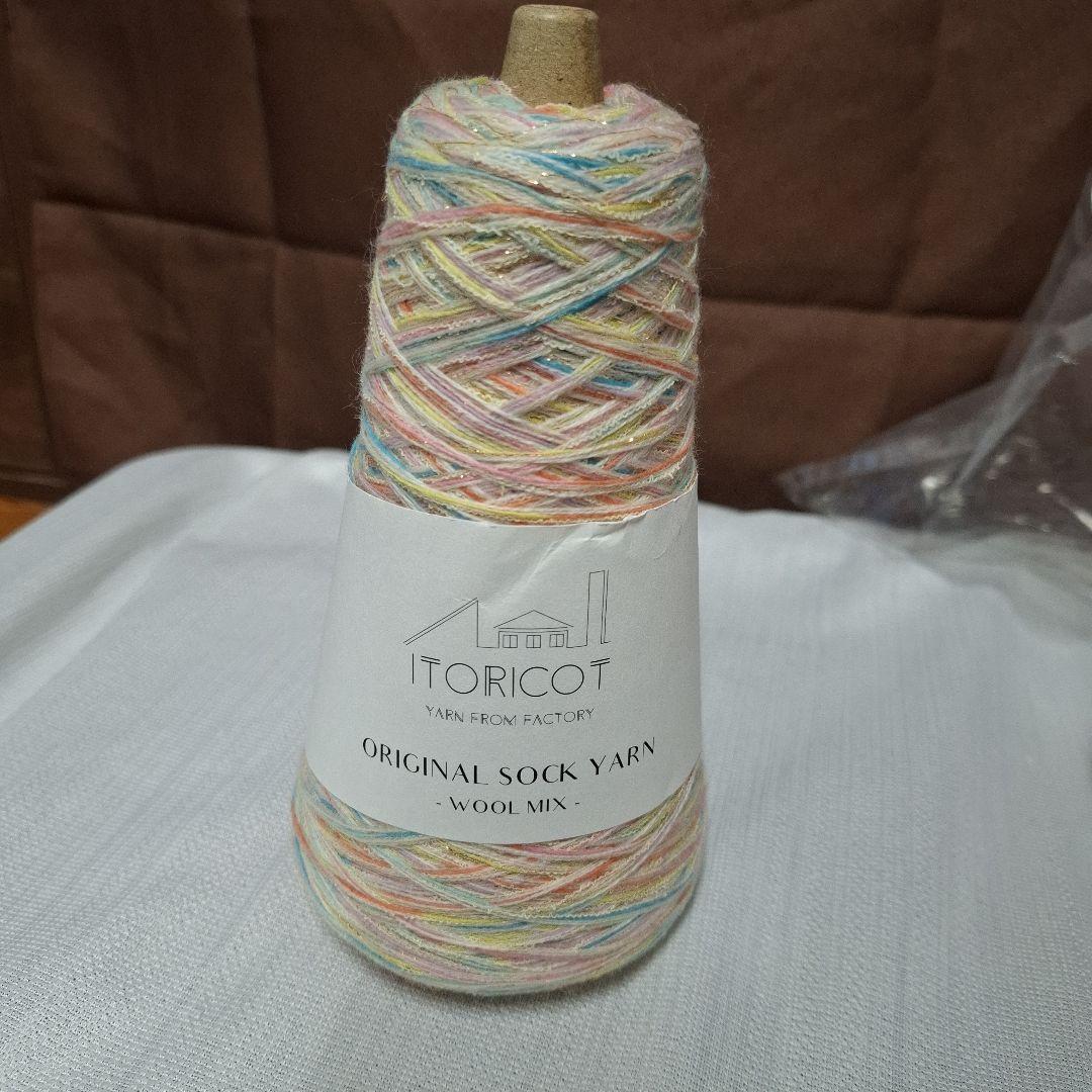 Cone of multicolored sock yarn with a white label reading ITORICOT ORIGINAL SOCK YARN - WOOL MIX on a white fabric surface.