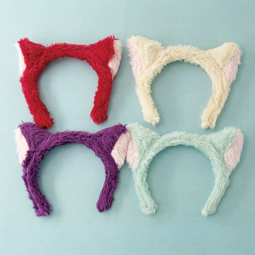 Four fluffy cat-ear headbands in red, cream, purple, and mint displayed on a light blue background.