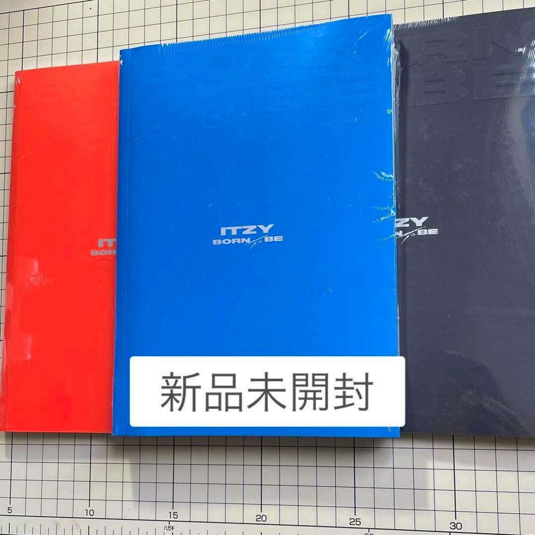 Three sealed ITZY "BORN TO BE" CD album packages in red, blue, and black on a gridded surface with a "新品未開封" sticker.