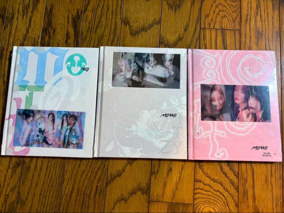 Three ITZY "MOTTO" albums displayed side by side on a wooden floor.