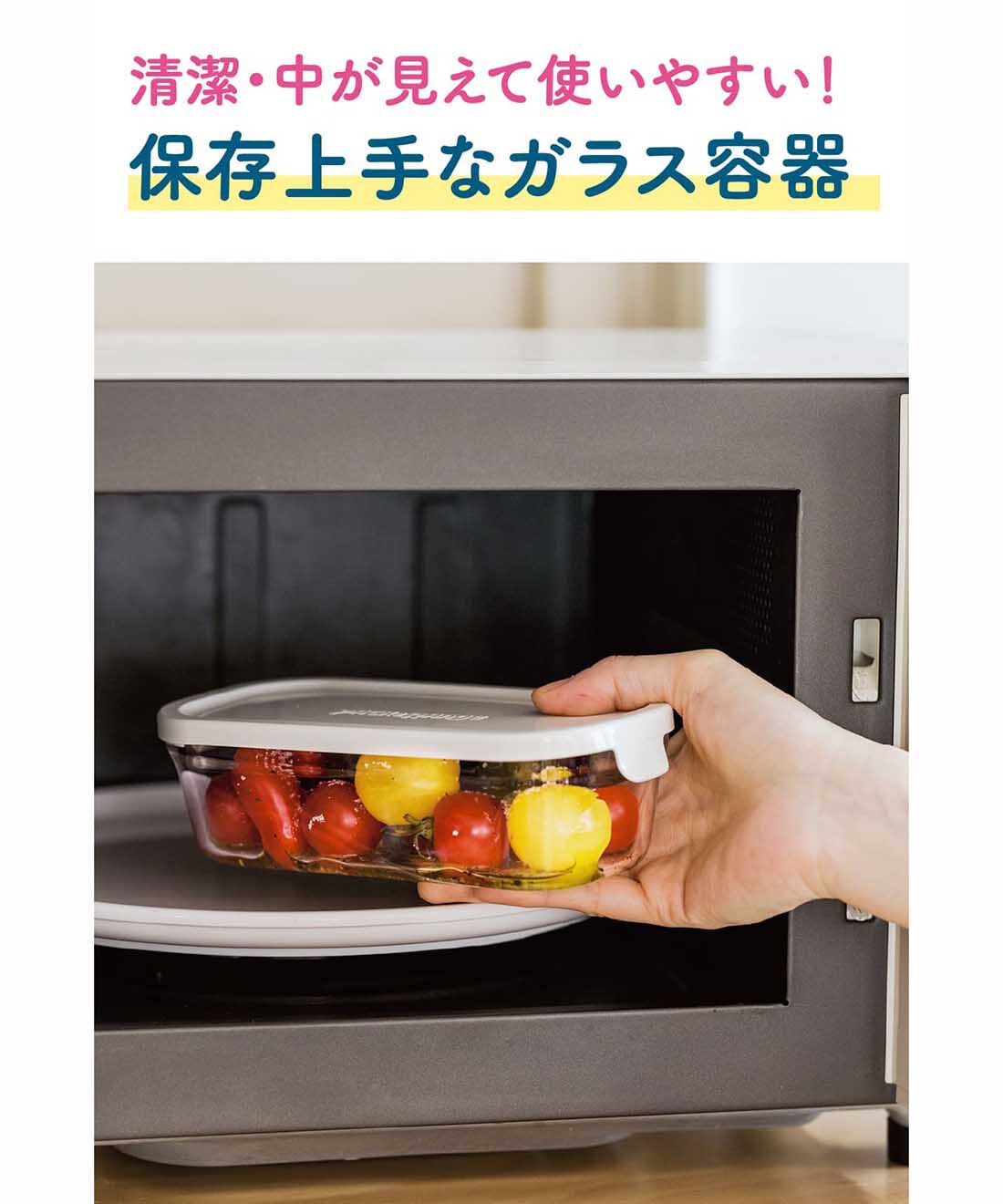 A hand placing an iwaki 500ml glass food storage container with a white lid into a microwave.