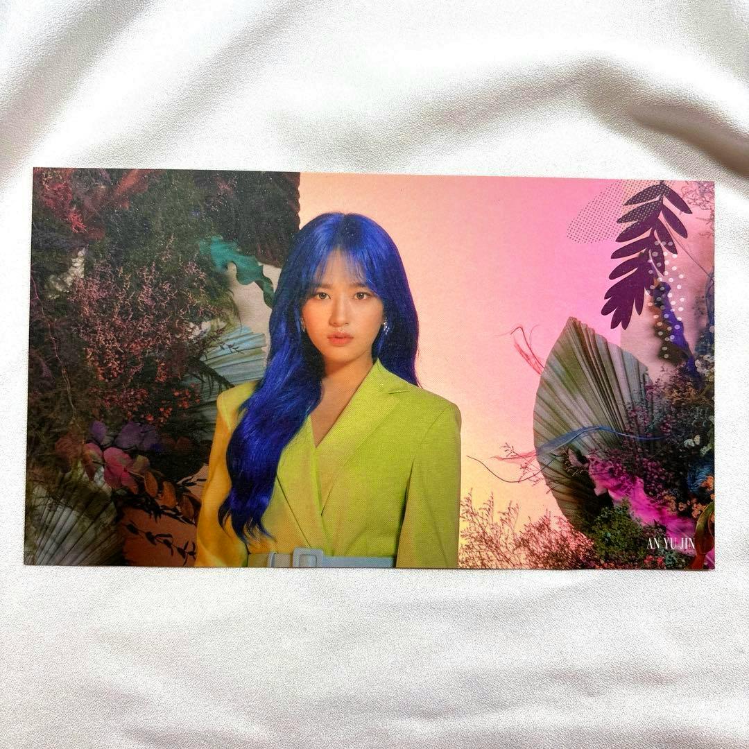 Front of a photocard showing a person with long blue hair wearing a lime-green blazer against a floral pink floral background, placed on white fabric.