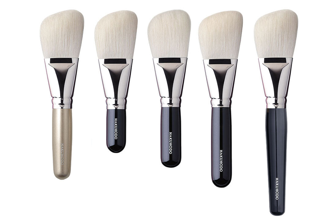 Five tapered eye shadow brushes with white bristles and different colored handles arranged in a row.