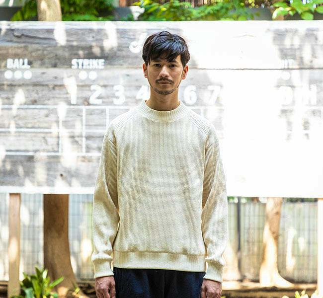 A man modeling the Jackman JM7200 waffle midneck sweater in a light cream color while standing outdoors.