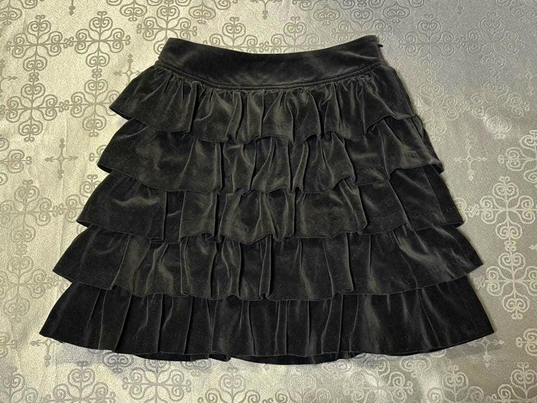 JaneMarple black five-tier ruffled velvet mini skirt laid flat on a patterned surface.