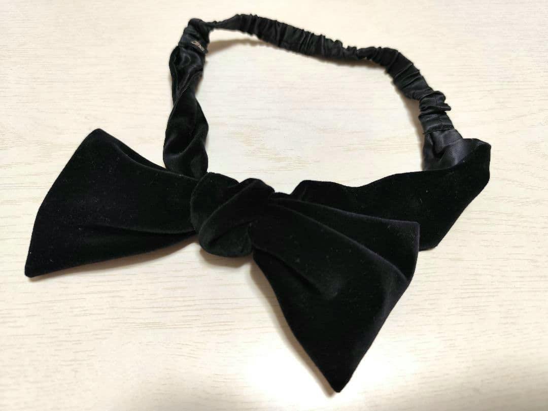 Black velour ribbon headband with a tied bow laid flat on a light wood surface.