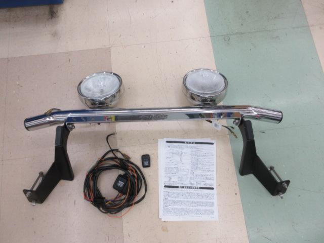 JAOS front skid bar with two round lights, two mounting brackets, wiring harness, remote, and instructions laid out on a floor.