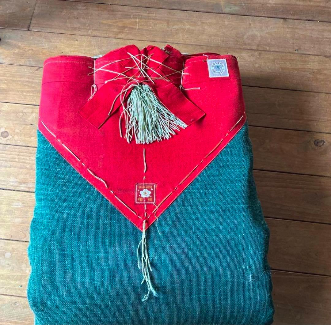 Folded green mosquito net with a red triangular decorative top and tassel placed on a wooden floor.