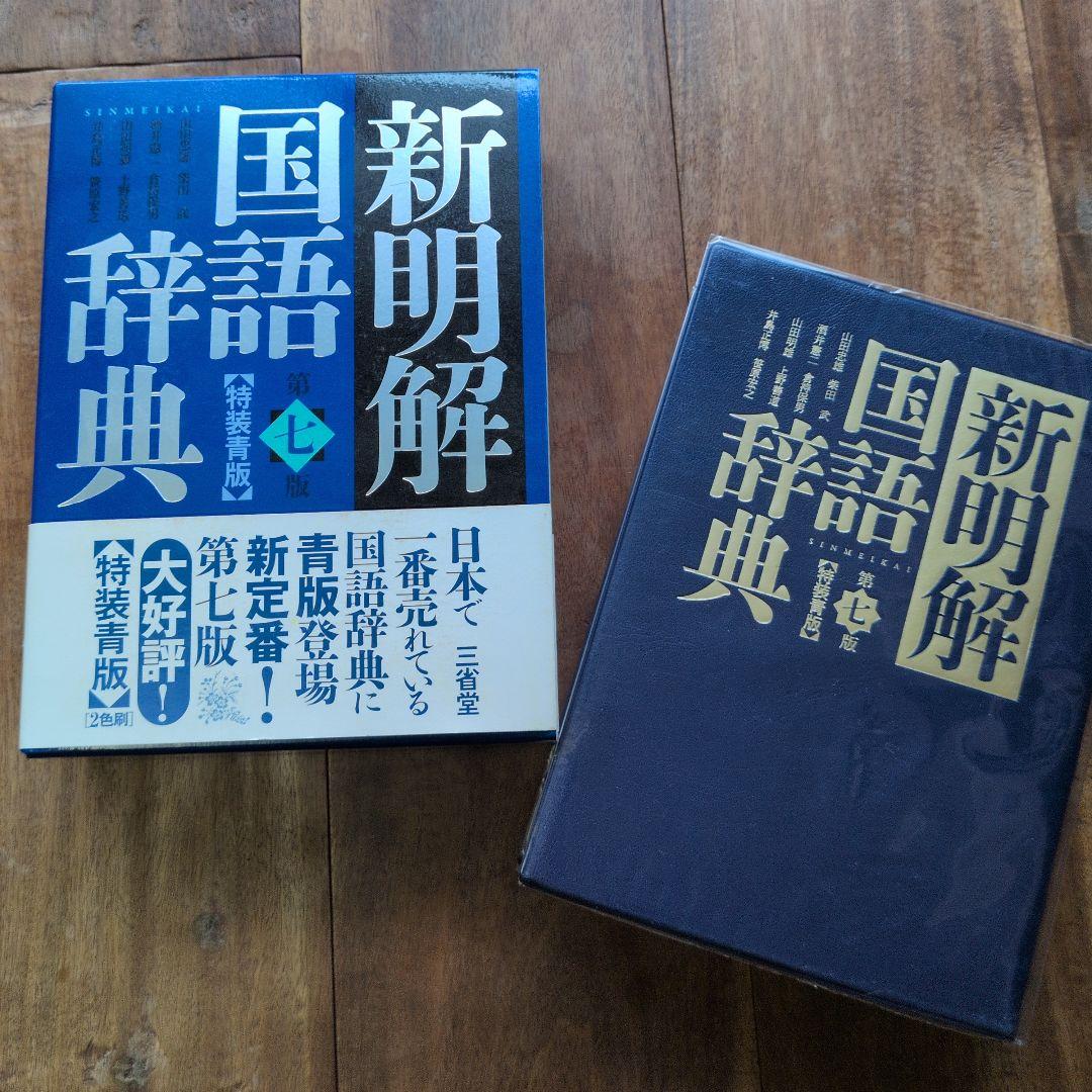 A copy of the Japanese dictionary 新明解国語辞典 第七版 特装青版 displayed next to its blue slipcase on a wooden surface.